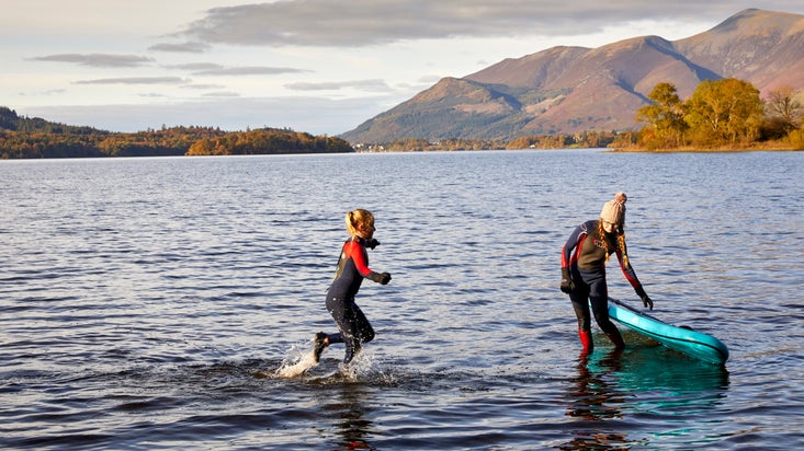 Two children in wetsuits playing with a paddle board in the lake